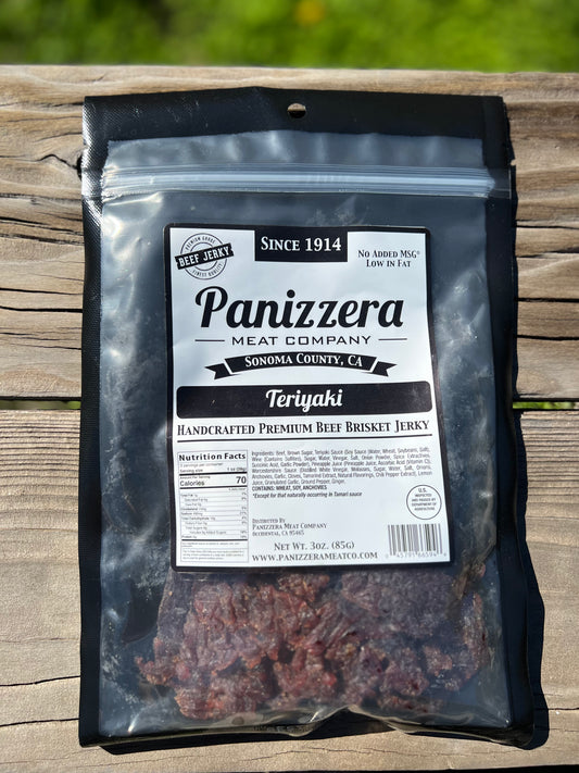 Panizzera Meat Company Teriyaki beef jerky package on a wooden surface with grass in the background